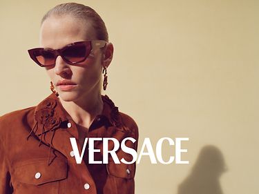 Versace Printemps-Été 2025 -Lara Stone porte les nouvelles lunettes de soleil œil-de-chat géométriques de Versace en rouge uni, disponibles en avant-première chez Sunglass Hut.